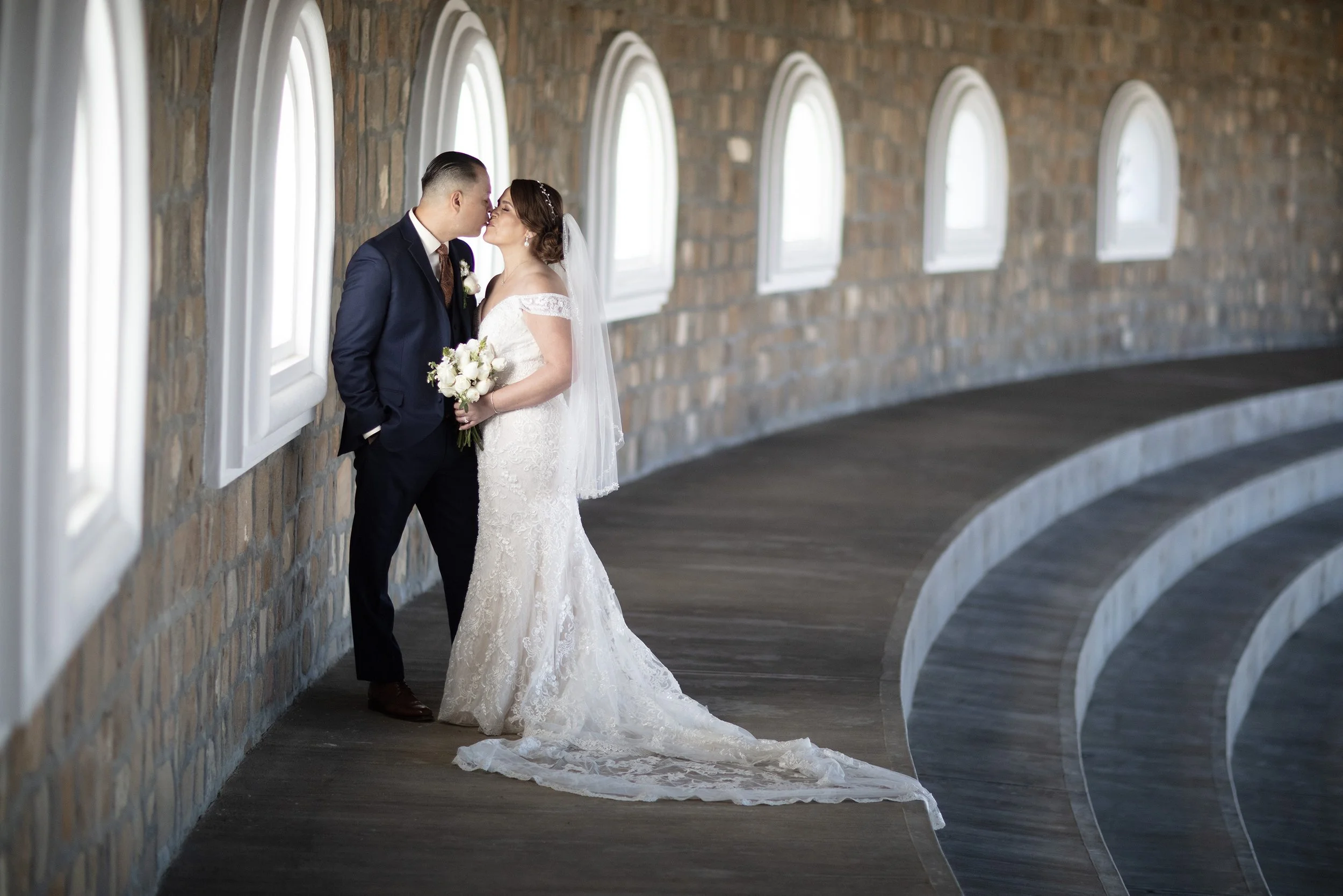 Bride in train and veil holding flowers kissing groom in beautiful stone building