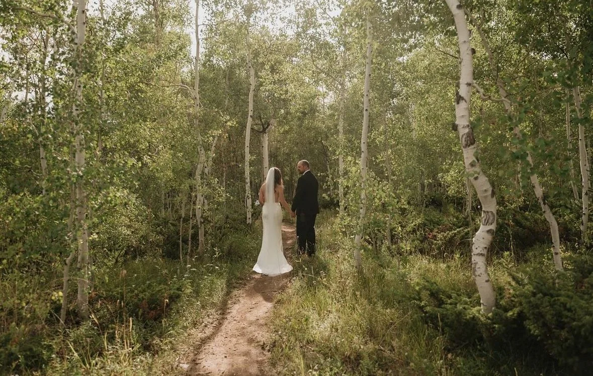 Bride and groom walking in forest with trees around.