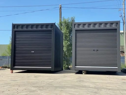 Two grey metal 10ft shipping containers with closed roll-up doors, placed on a concrete surface outdoors.