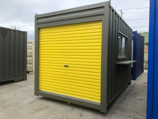 A modified shipping container with a yellow roller door and small window with a black shelf outside.