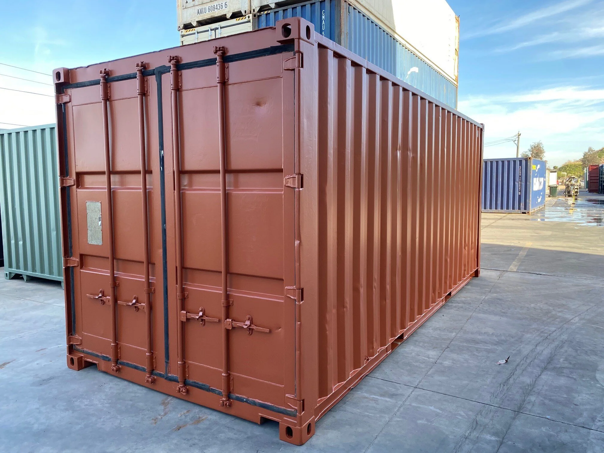 A red shipping container in an outdoor storage yard with other containers visible in the background.