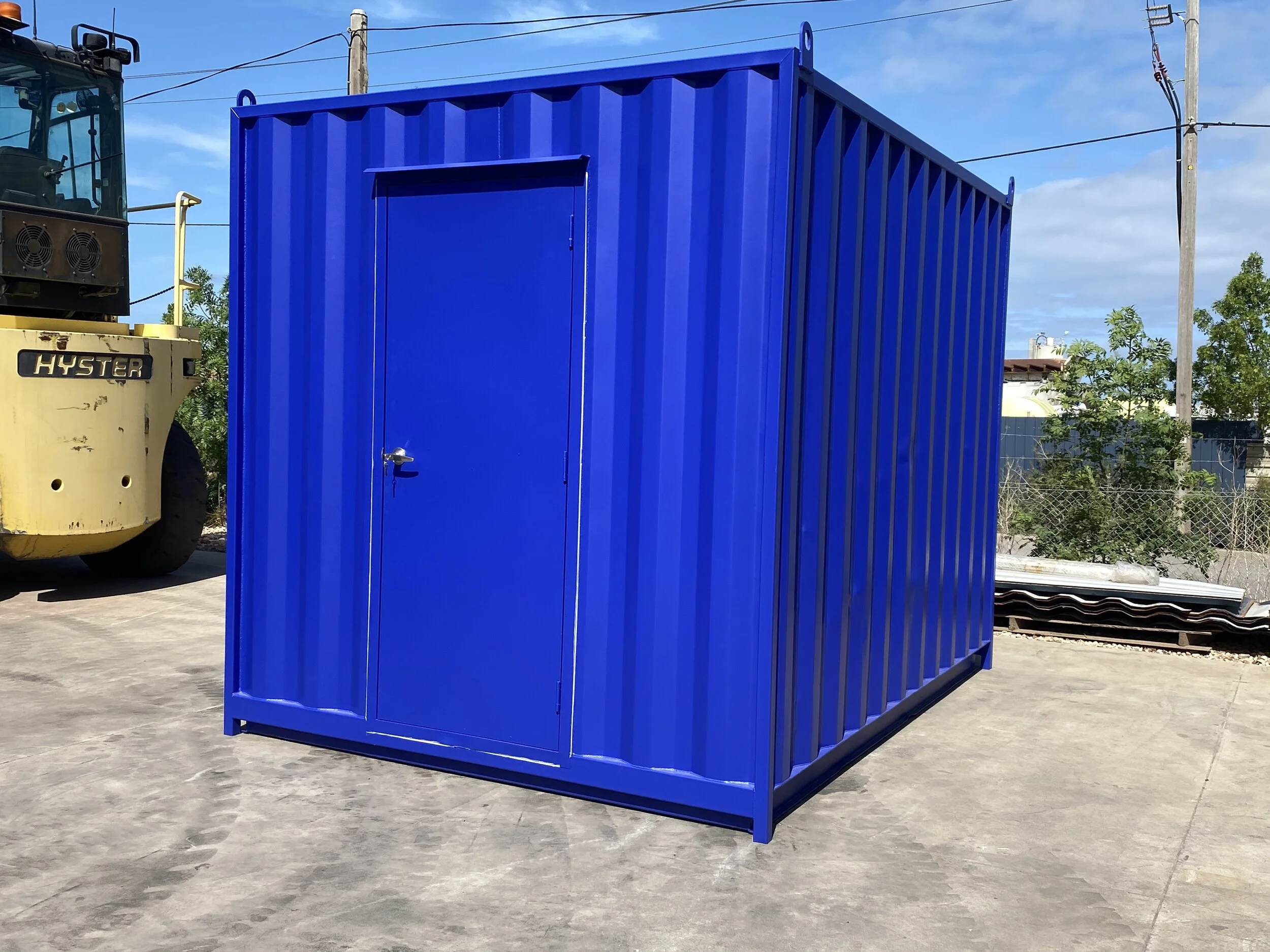 10ft Blue shipping container with access door, set outdoors on concrete, with a yellow forklift and trees in the background under a partly cloudy sky.