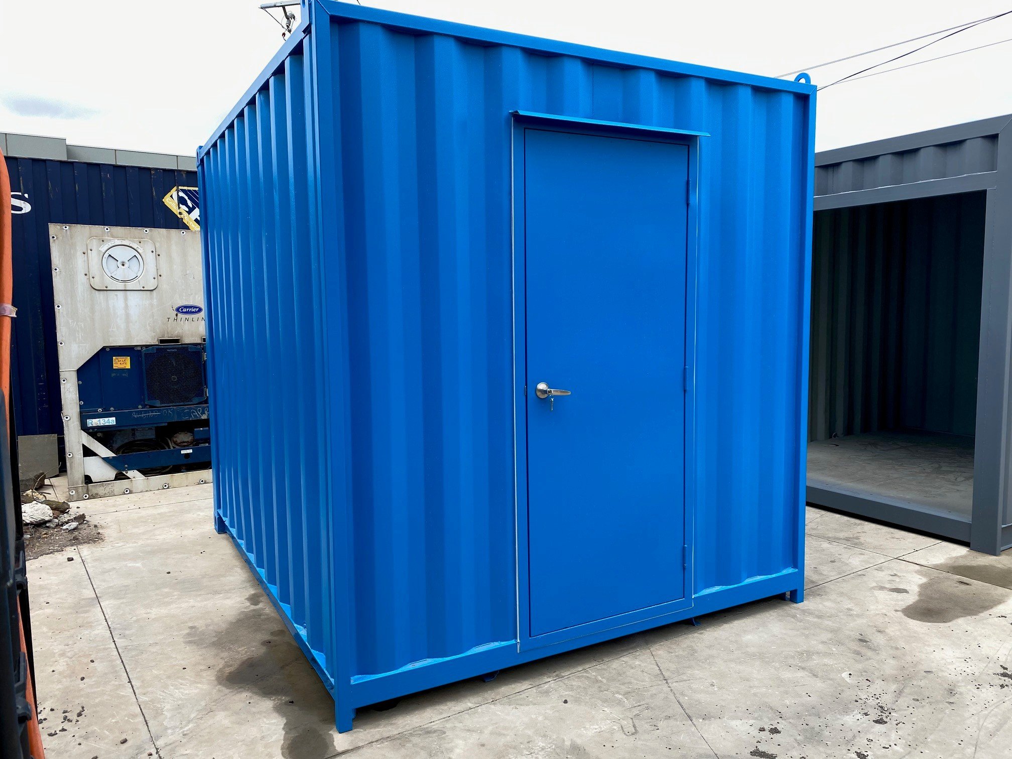 A customsize bblue shipping container shed with a personal access door, situated outside on concrete ground