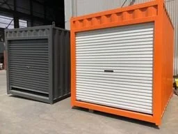 Two large shipping containers or storage units, one black and one orange, with roll-up doors, placed outdoors on a paved surface.