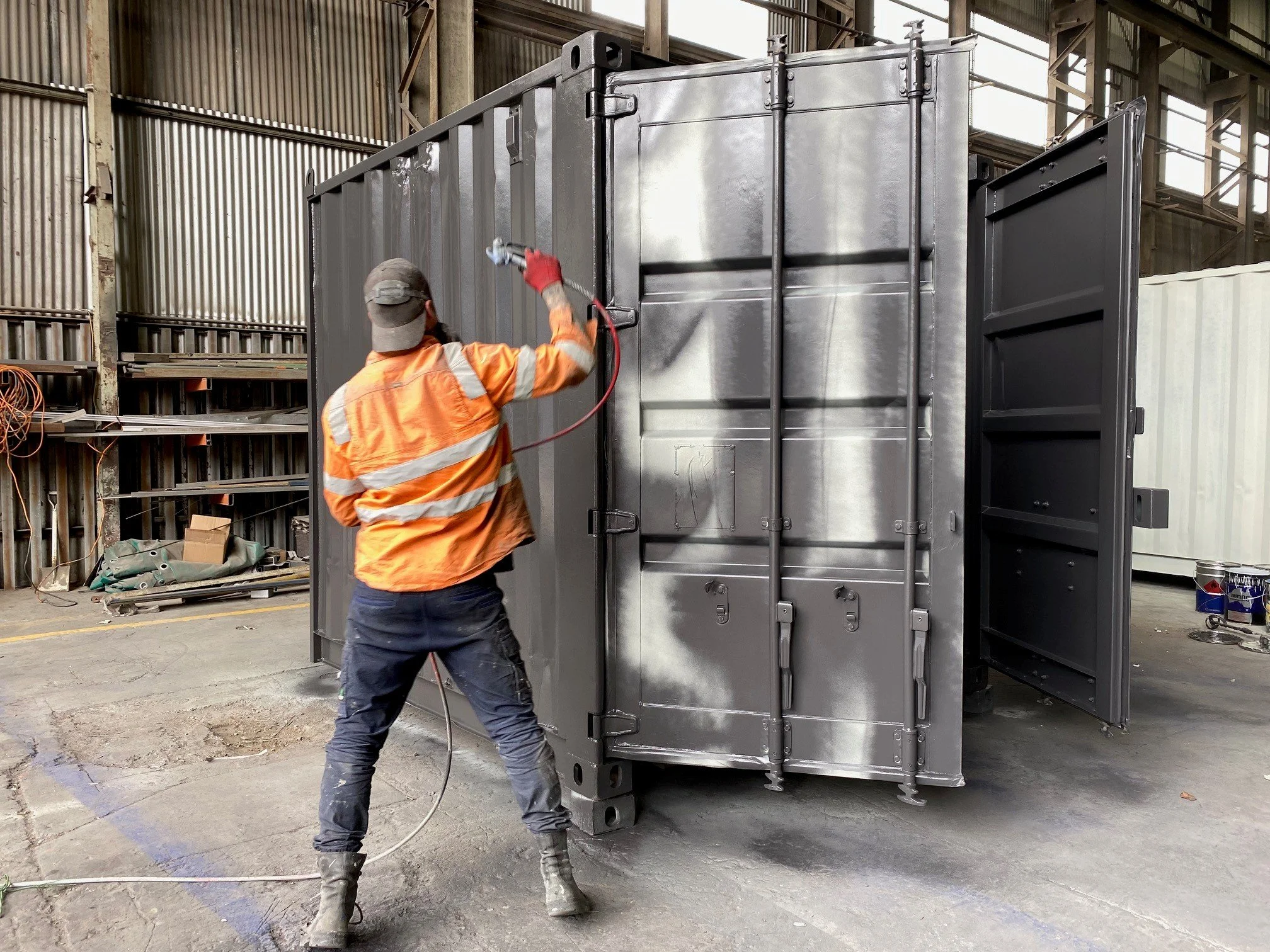 Worker in orange safety jacket spray painting a 20ft shipping container