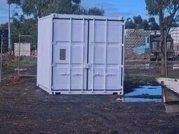 A 10ft white shipping container turned into a small pavilion or cooking area with an open front and a small fire pit or grill on the ground.