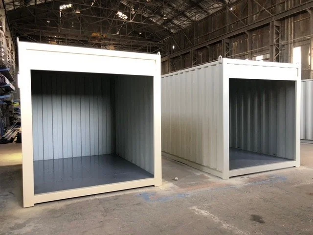 Two white shipping containers with open doors, located inside a warehouse or industrial building.