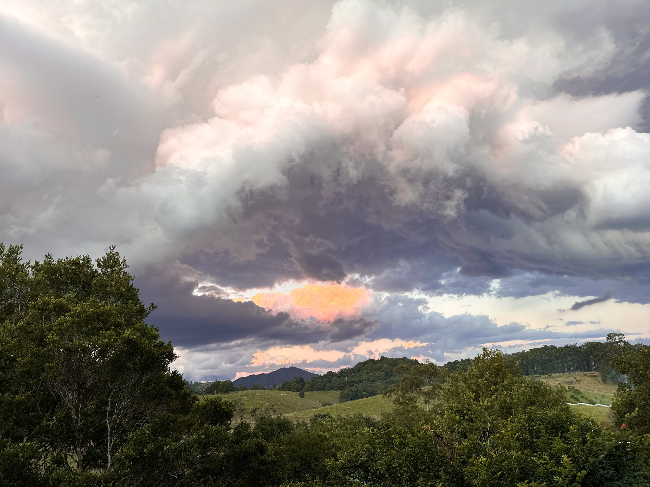 Dramatic cloudy sky over a lush green landscape with hills and trees.