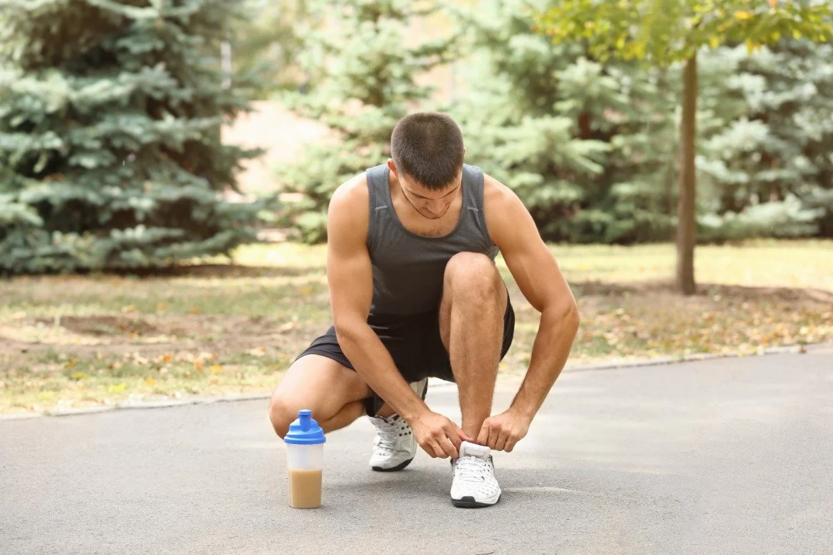 Man with protein shake. He's tying his shoelaces