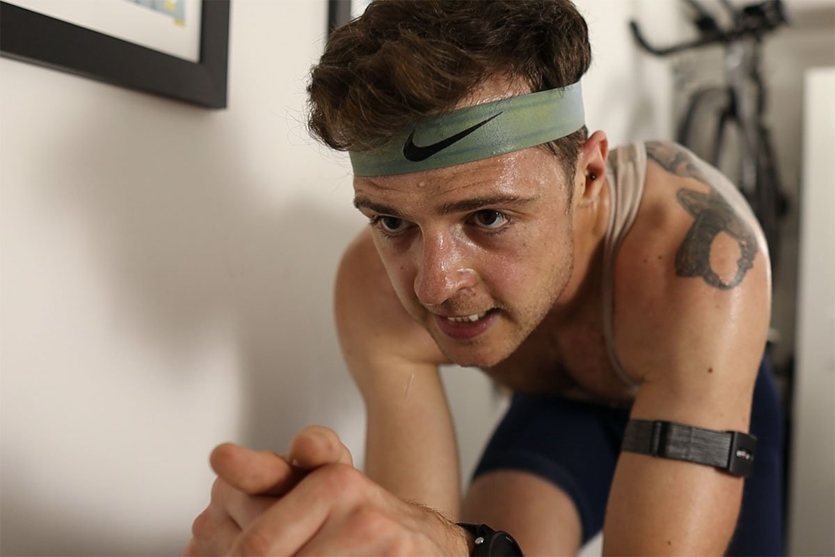 A sweaty athlete wearing a headband leans forward intensely during an indoor cycling workout.