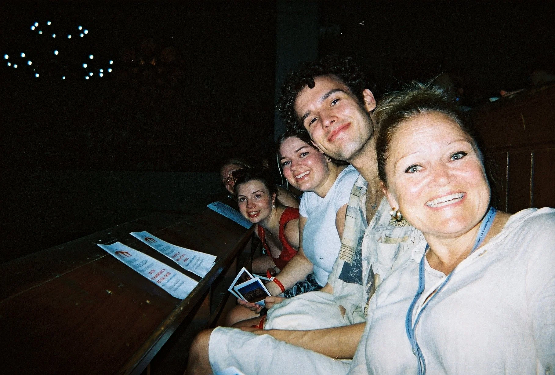 En gruppe mennesker som smiler og poserer for kameraet i en mørk rom, sannsynligvis på en konsert eller arrangement.