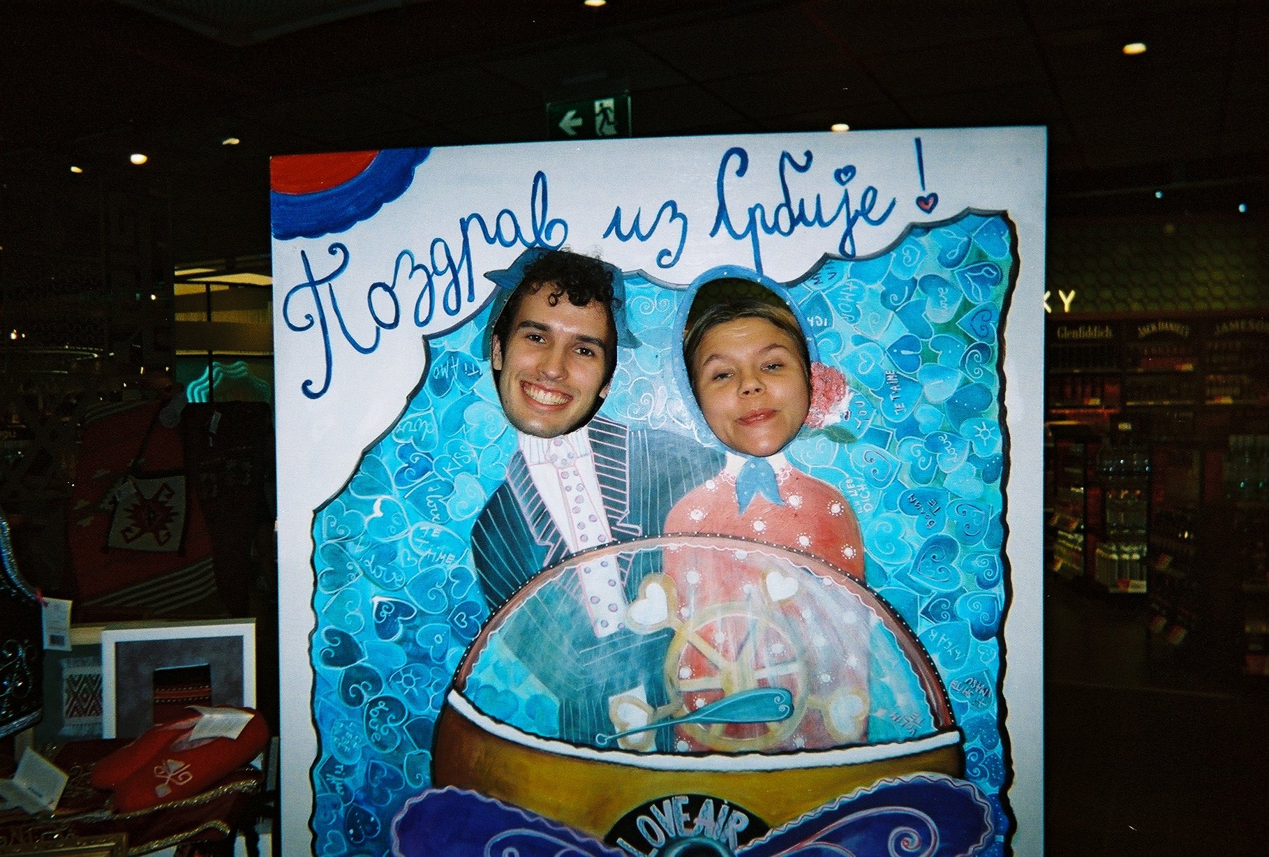 To personer med ansiktsuttrykk står bak en utklippet ramme med ansiktene deres, som er plassert over tegning av to personer i bryllupsklær. Tekst på rammen sier 'Hoppas på utgifte!'