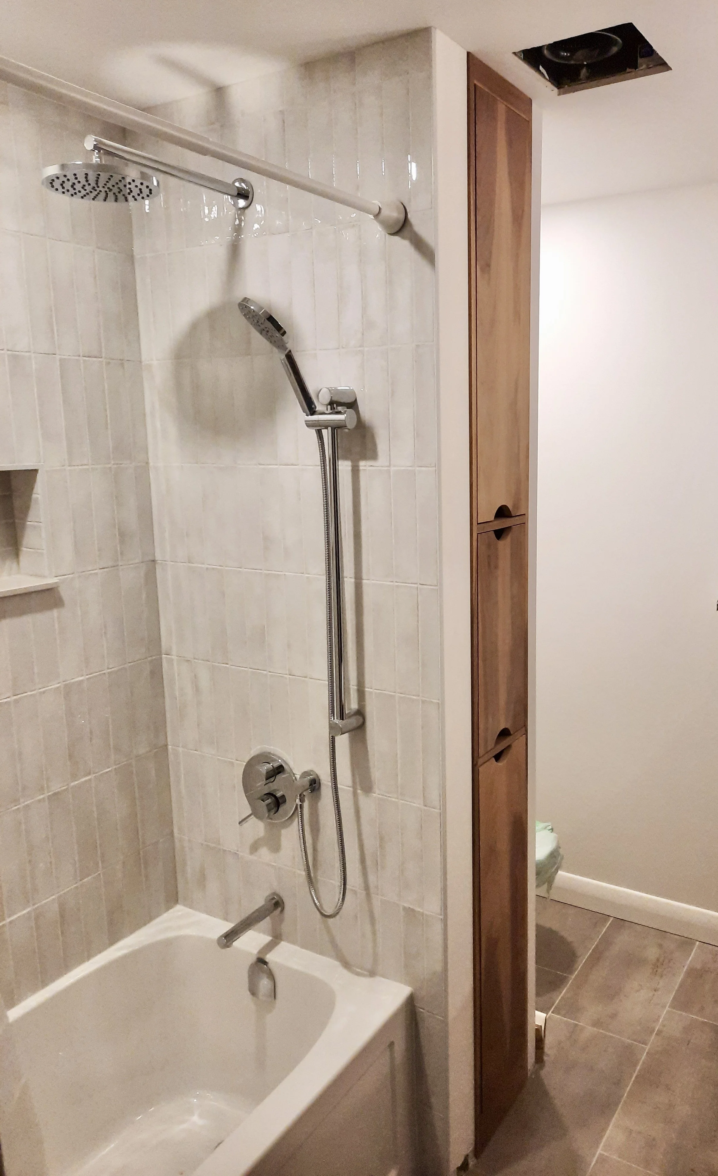 Bathroom shower area with two showerheads, a bathtub, and a partial view of a bathroom closet with brown doors.