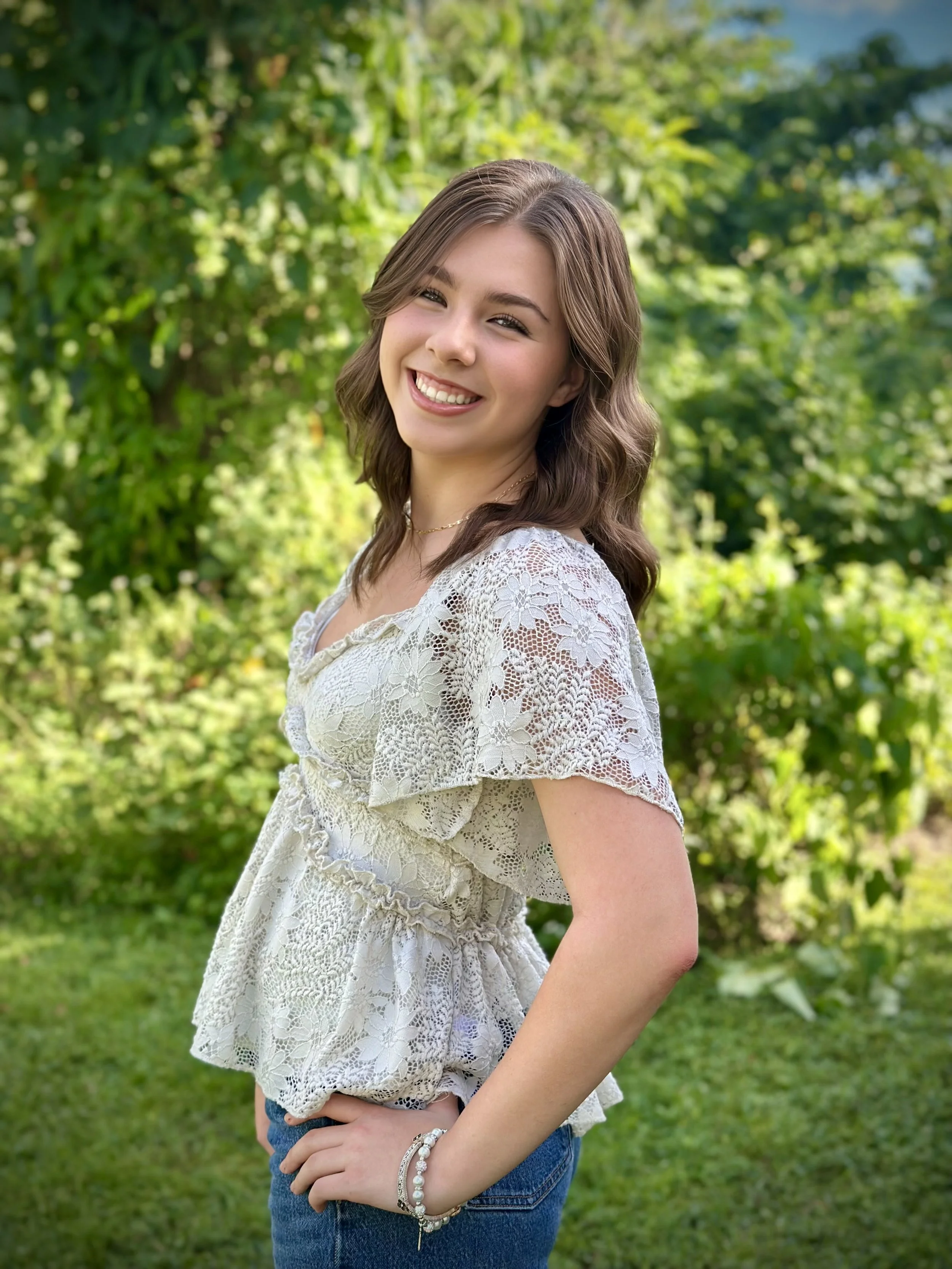 Girl in a white shirt posing outdoors with a forest background.