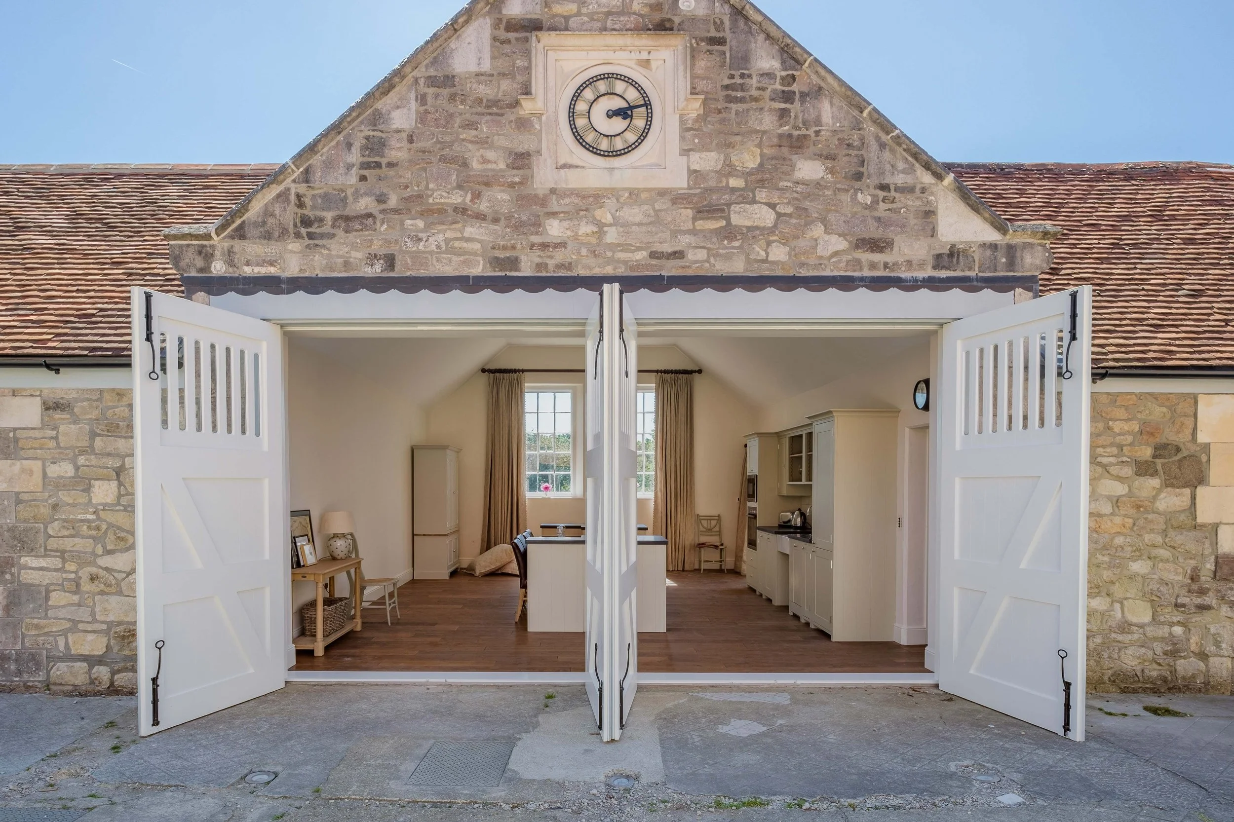 Converted coach house at Barton Manor Estate, with large white doors opening into the renovated interior accommodation.