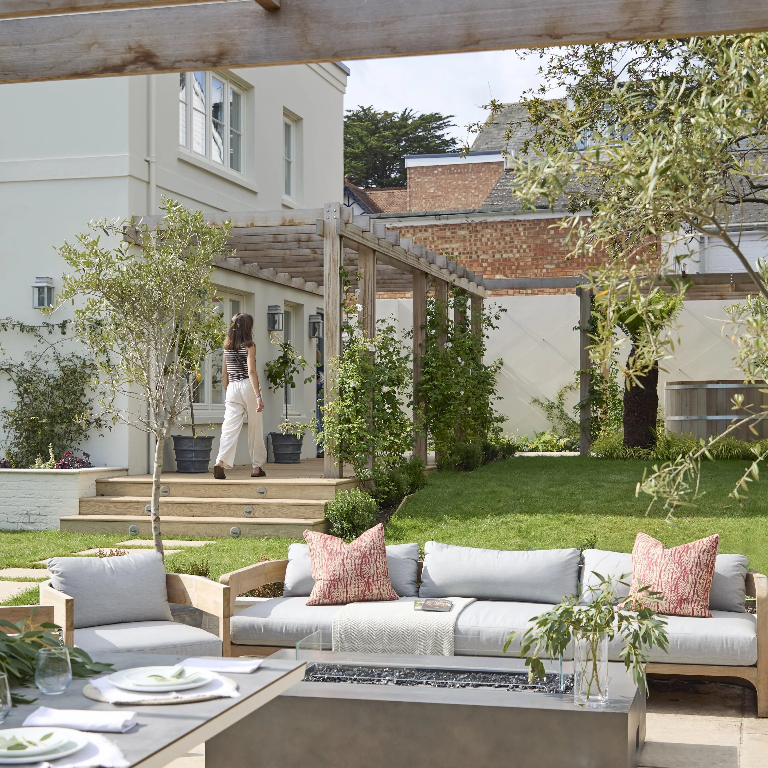 Timber pergola shading an outdoor seating area in the landscaped garden of Ellacombe, with pale rendered walls and traditional brick boundaries.