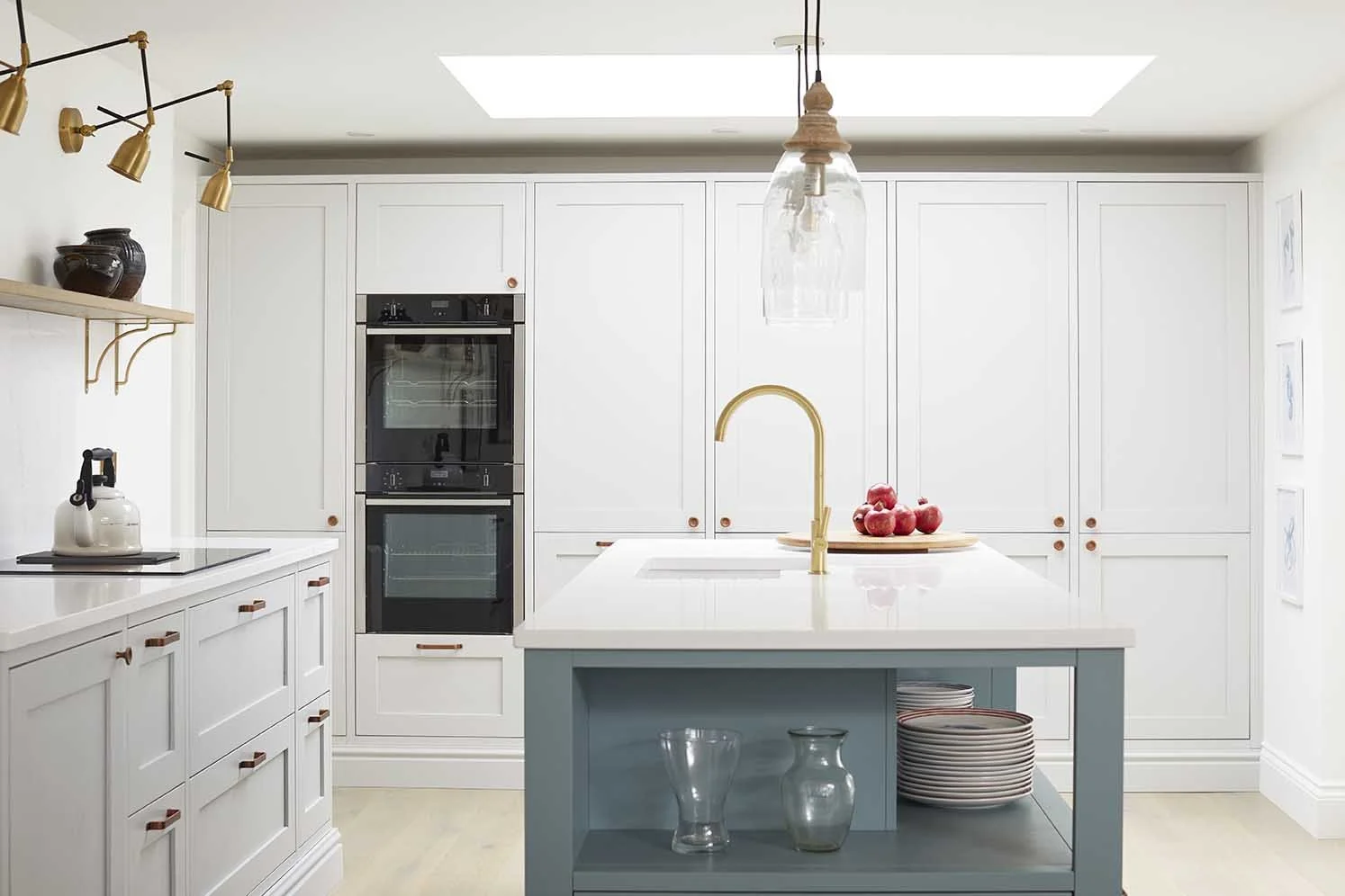 Bespoke white kitchen with a pale blue island, brass tapware, traditional-style cabinetry and a large rooflight bringing natural light into the space.