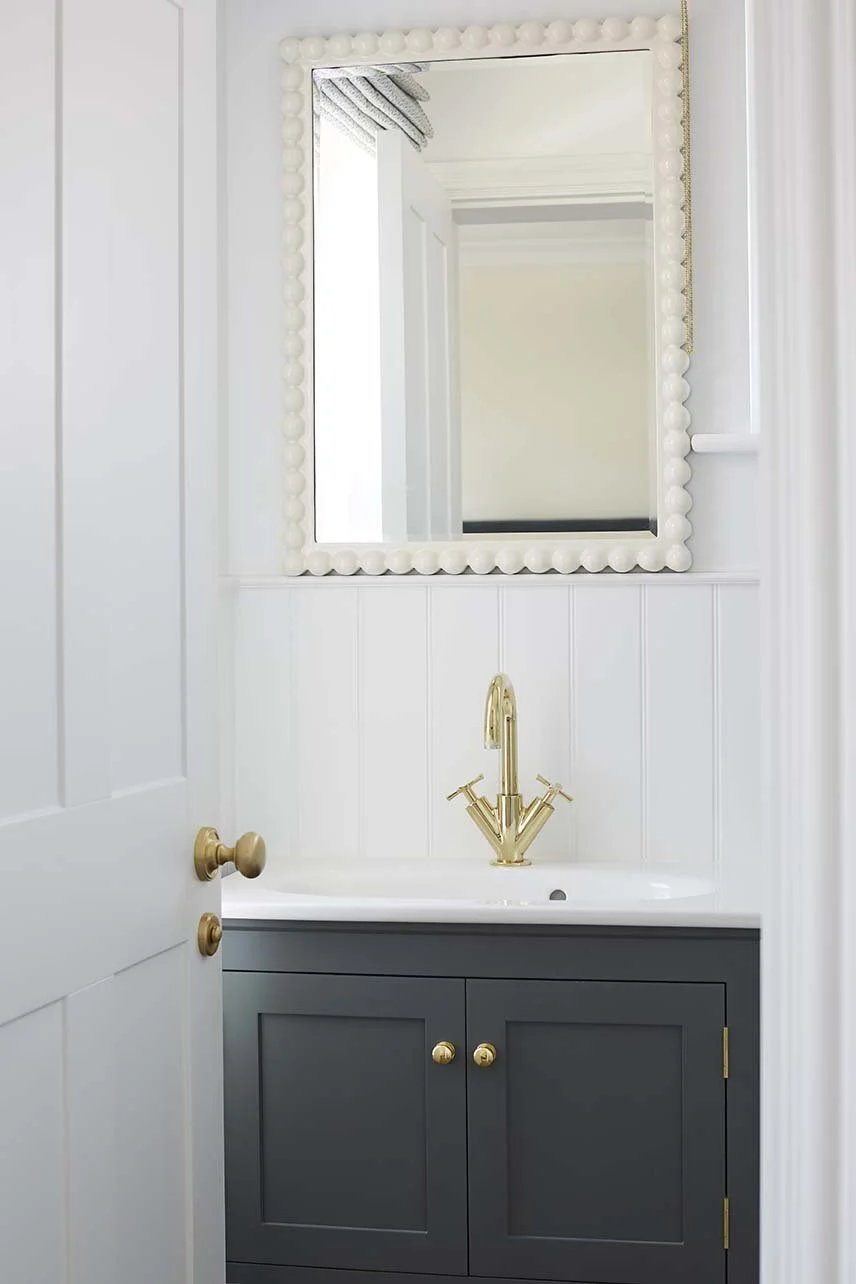 Bathroom vanity with dark blue cabinetry, a white basin, brass tapware and a decorative white-framed mirror.