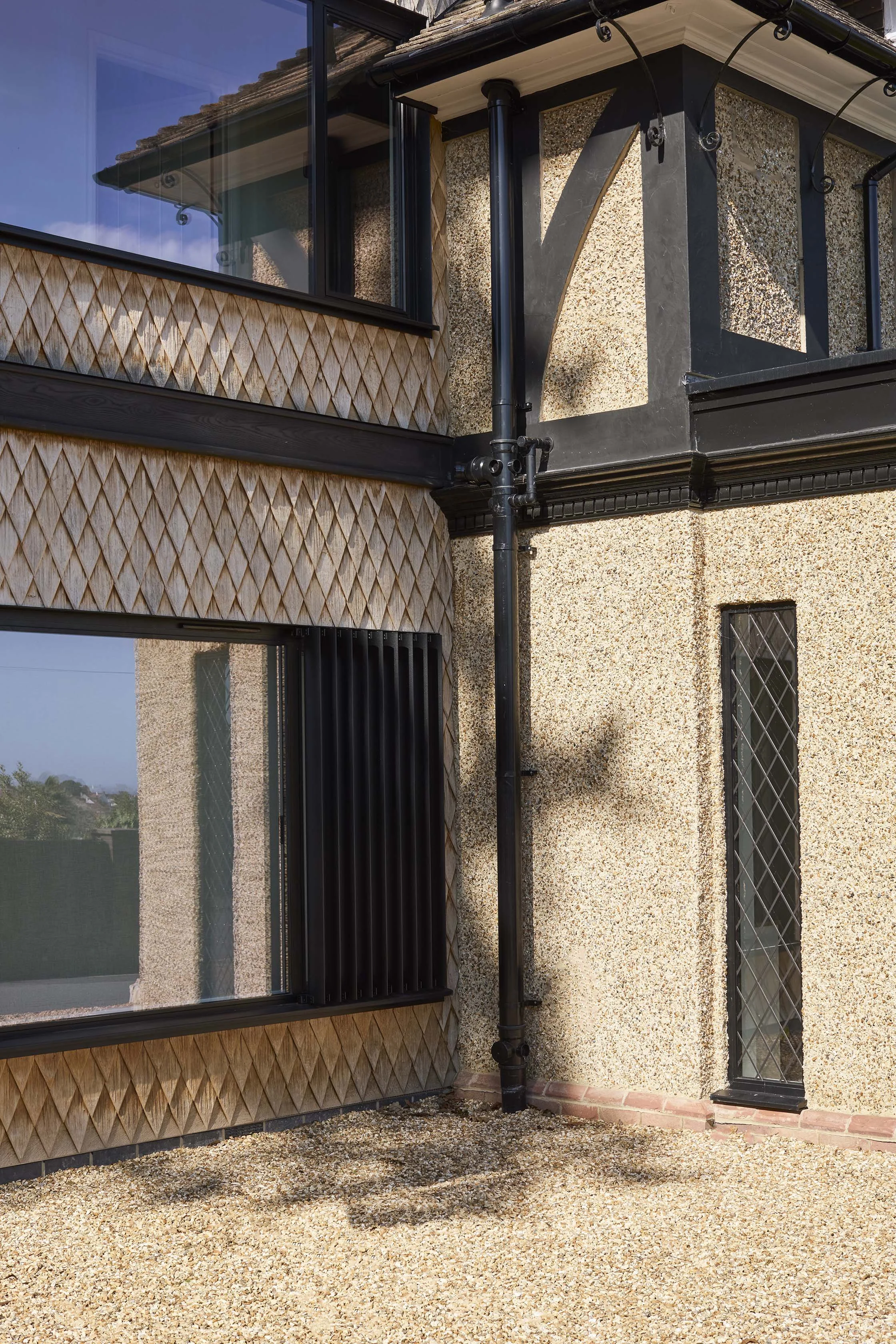 Detailed junction between diamond-pattern oak shingles, dark timber framing and the textured render of the original house.