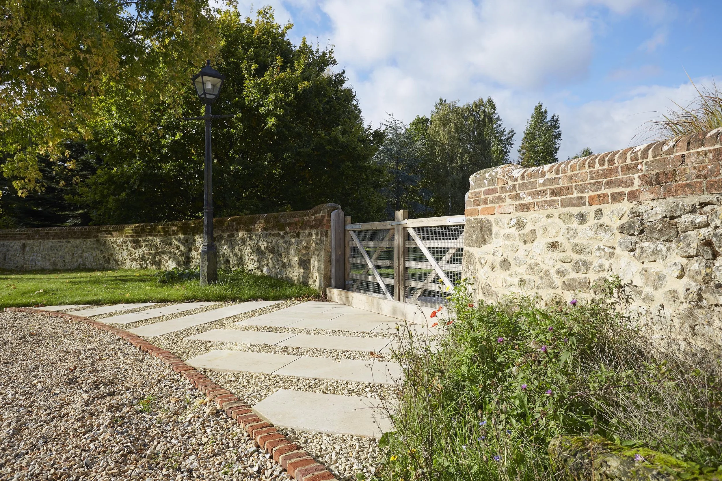 Farmhouse garden entrance with large stone paving slabs, gravel joints, brick edging, traditional stone boundary walls and timber gate.