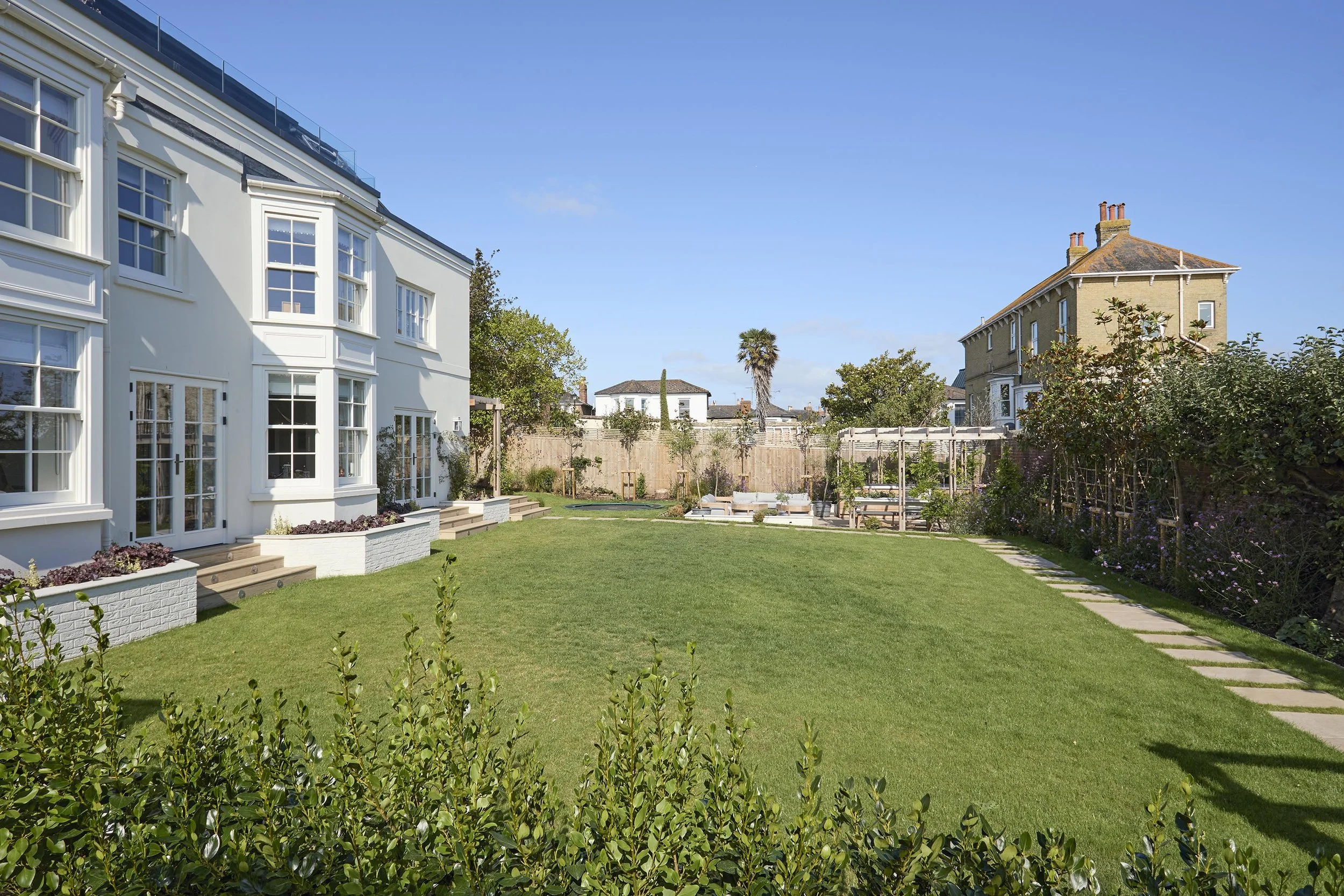 Renovated seaside home at Ellacombe, with a pale rendered rear elevation, glazed doors, lawn and planted garden enclosed by boundary walls.