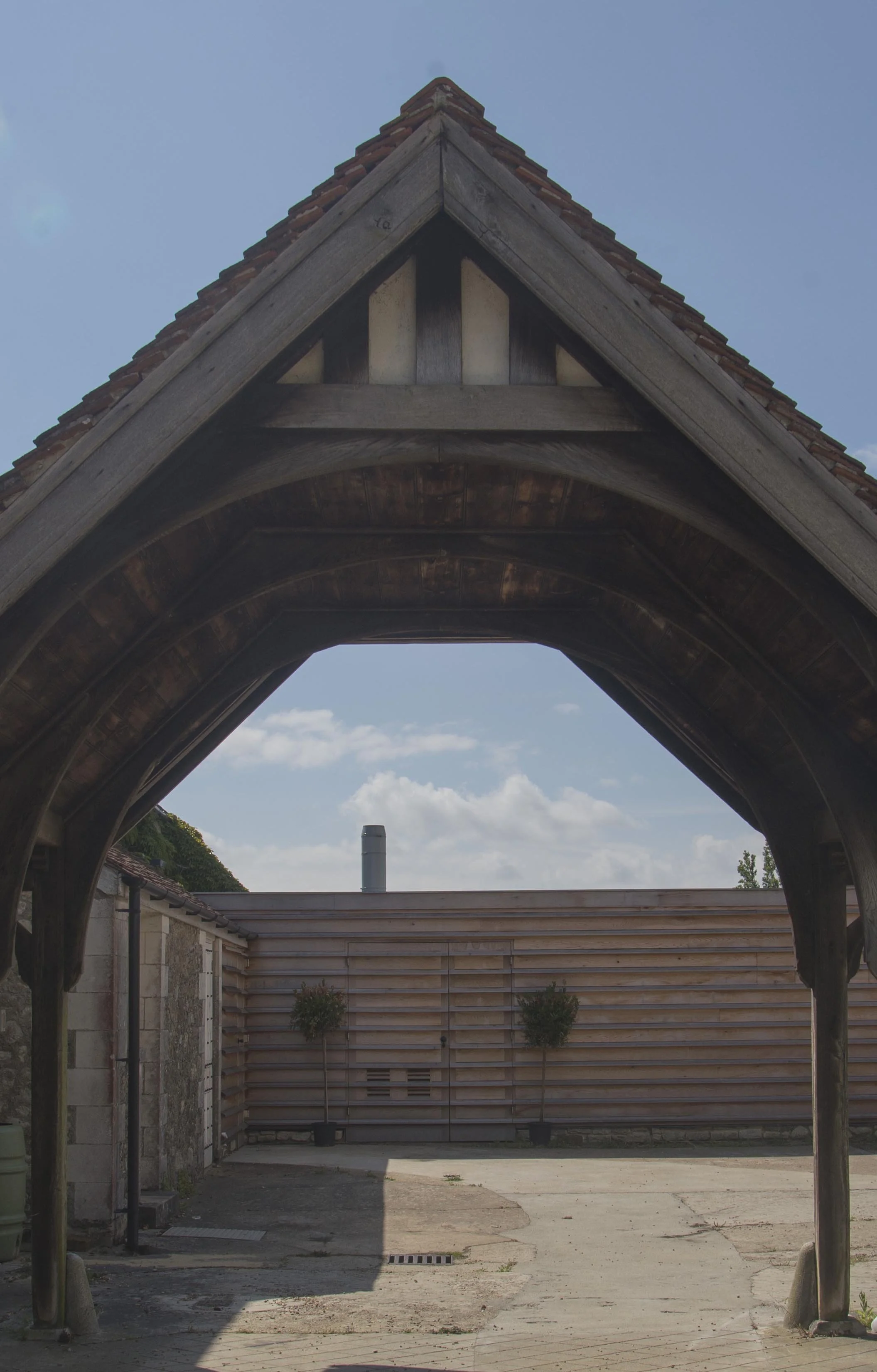 View through a traditional timber-framed covered passage at Barton Manor Estate towards a contemporary timber-clad courtyard wall.