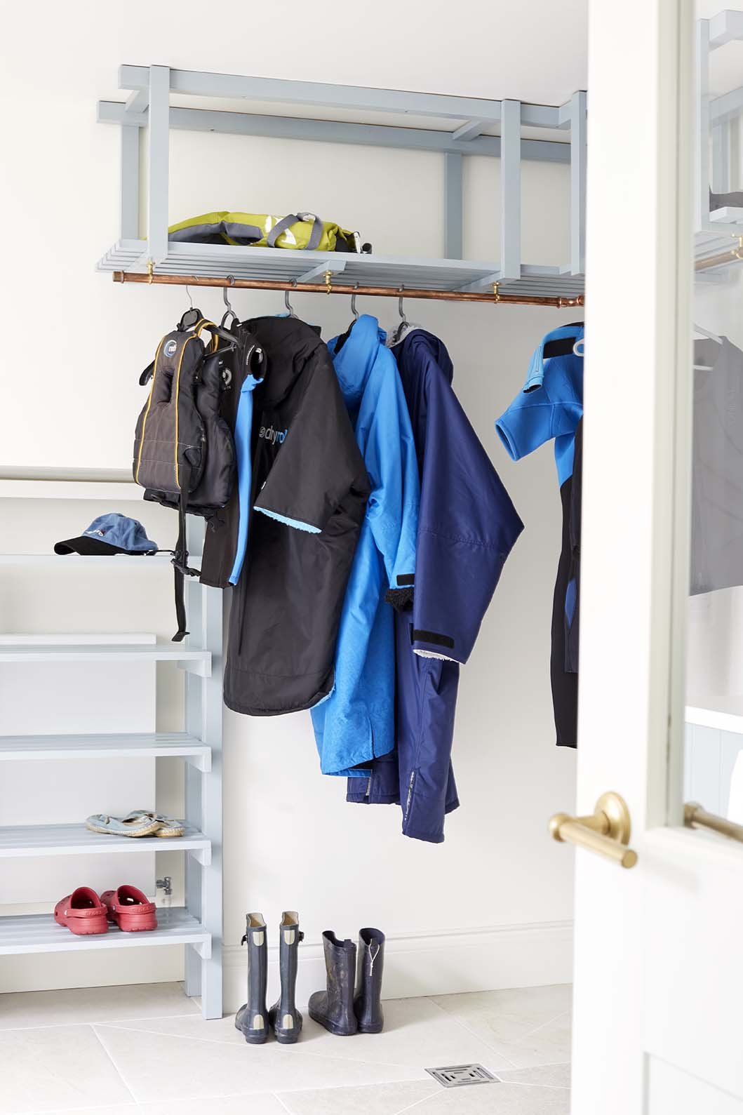 Purpose-designed drying and storage area with a copper hanging rail, pale blue shelving and wetsuits, providing practical space for seaside family living.