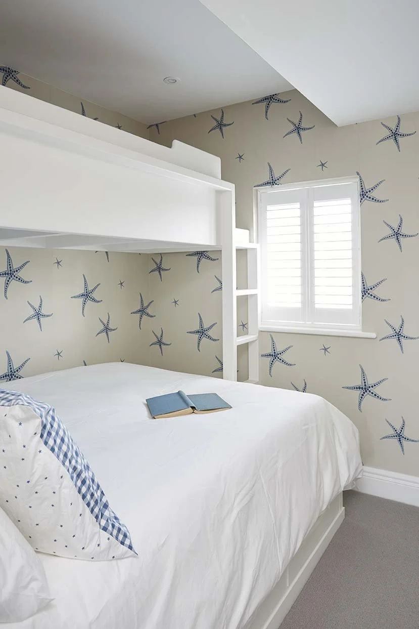 Children’s bedroom with a bespoke white bunk bed, integrated ladder and playful blue starfish wallpaper in a coastal-inspired interior.