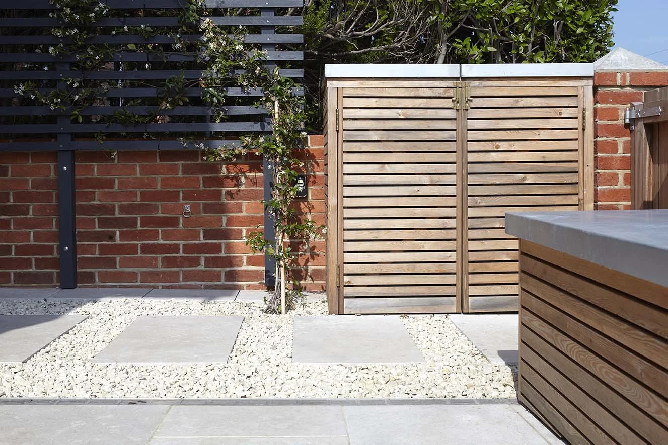 Contemporary timber garden gate and dark horizontal slatted screening against traditional red-brick walls, with pale gravel and stone paving.