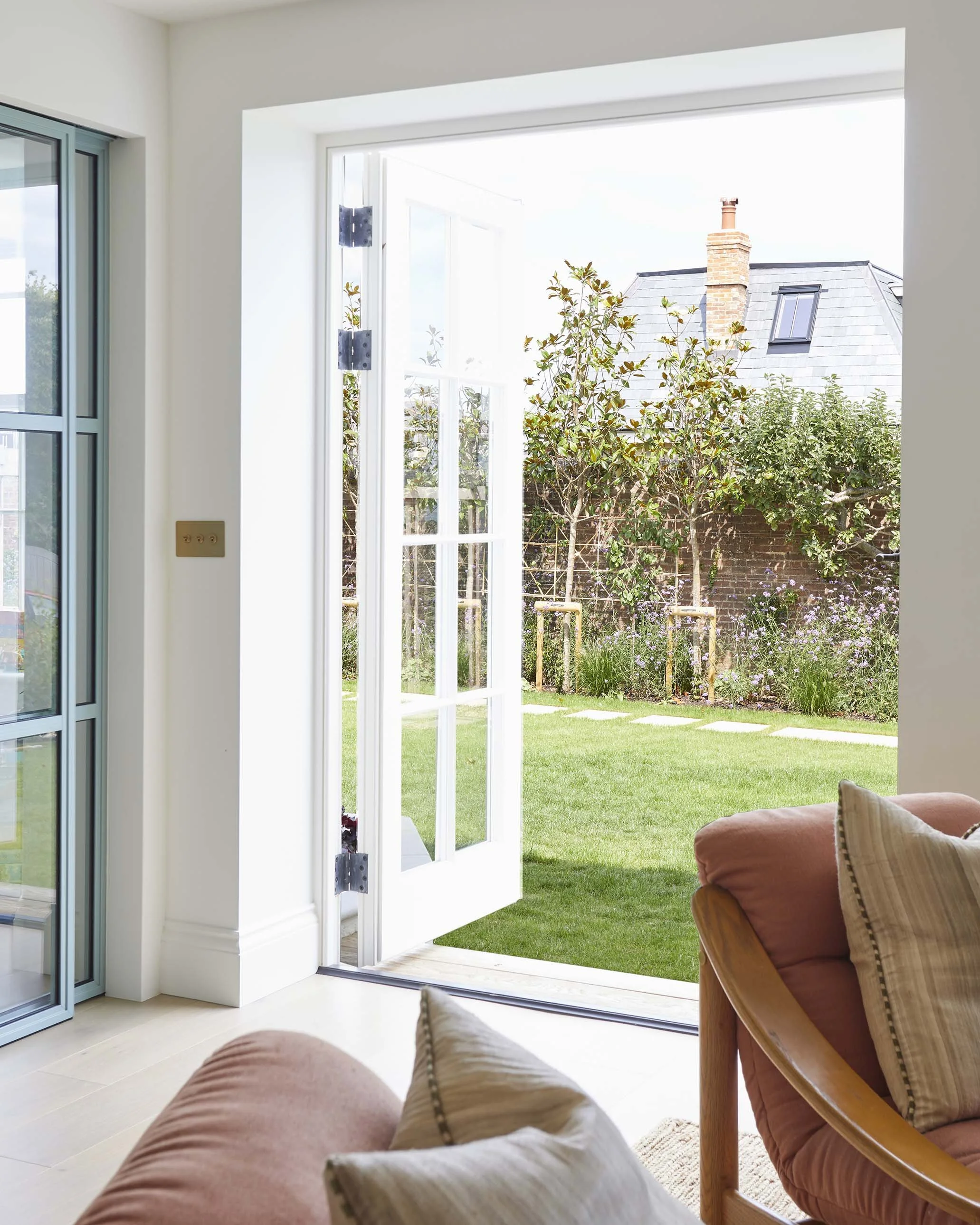 Living room with full-height glazed doors opening directly onto the lawn, connecting the renovated house with its private landscaped garden.