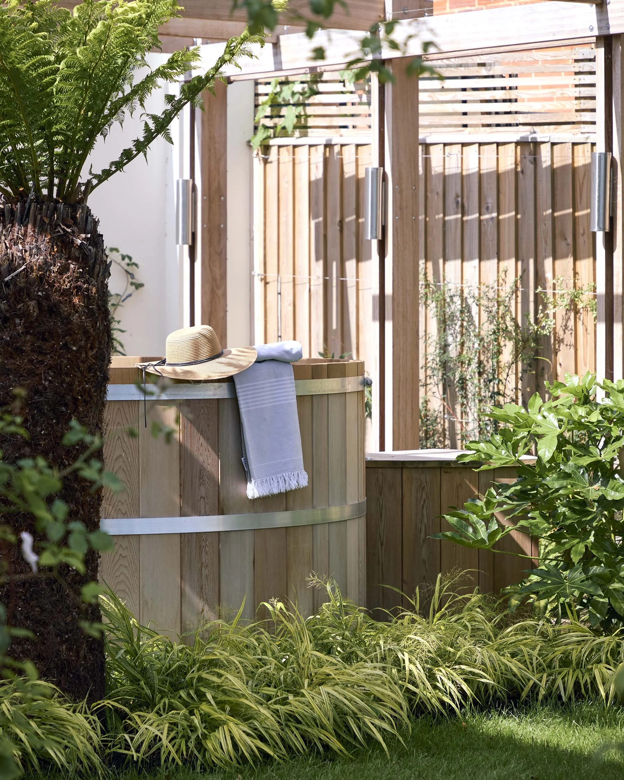 Wooden outdoor hot tub set within a private garden enclosure, surrounded by timber screening and lush planting at Ellacombe.