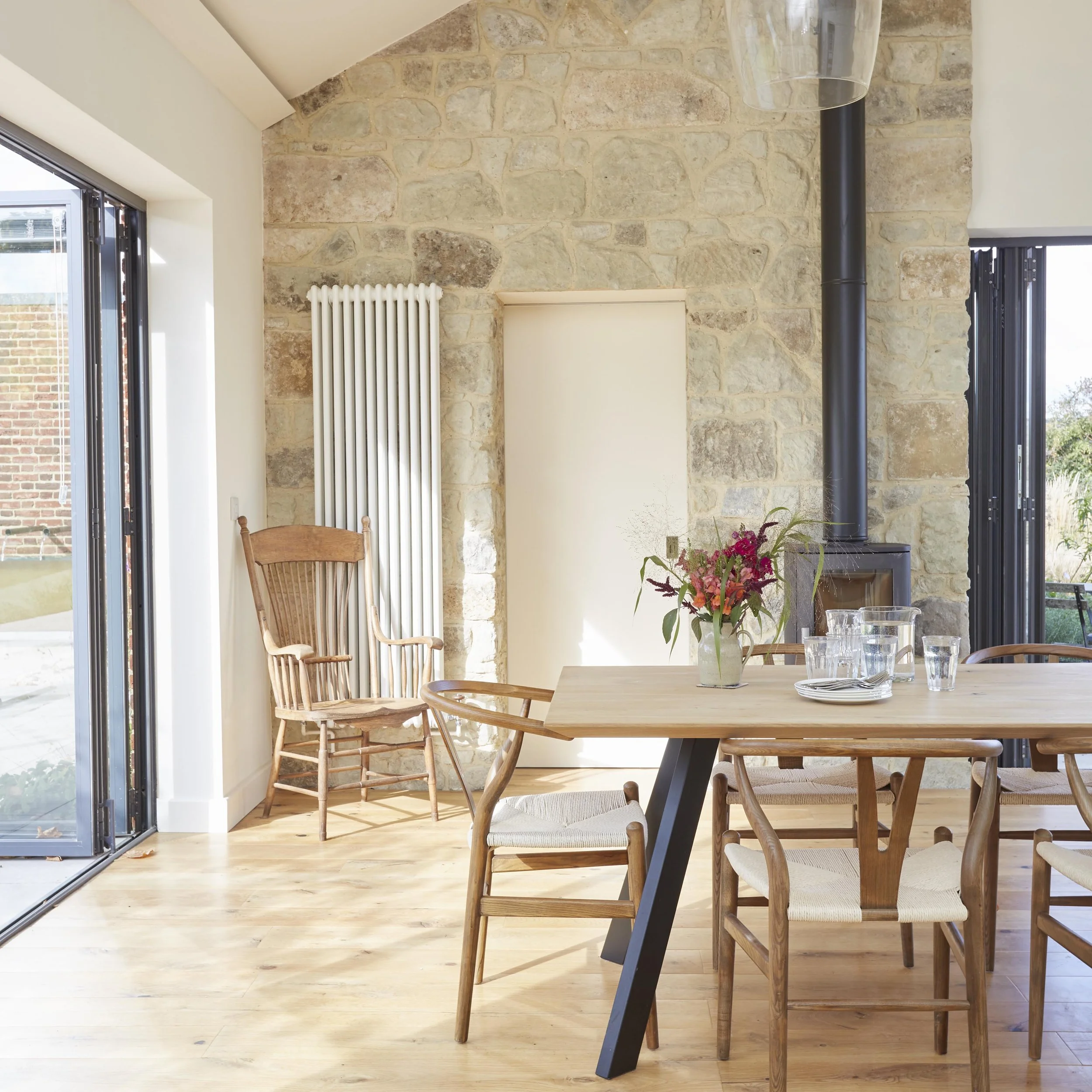 Farmhouse dining room with vaulted ceiling, exposed stone fireplace, timber dining table and large glazed doors opening onto the garden.