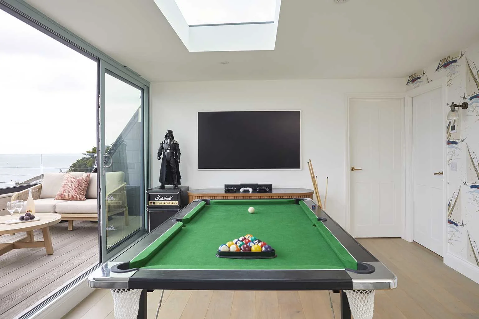 Bright games room with a green-felt pool table, rooflight and sliding glazed doors opening onto the sea-view roof terrace.