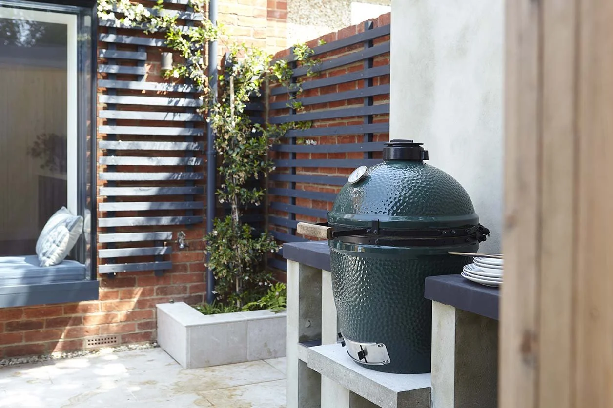 Outdoor cooking area with a built-in worktop, ceramic barbecue and dark slatted timber screening beside the landscaped courtyard.