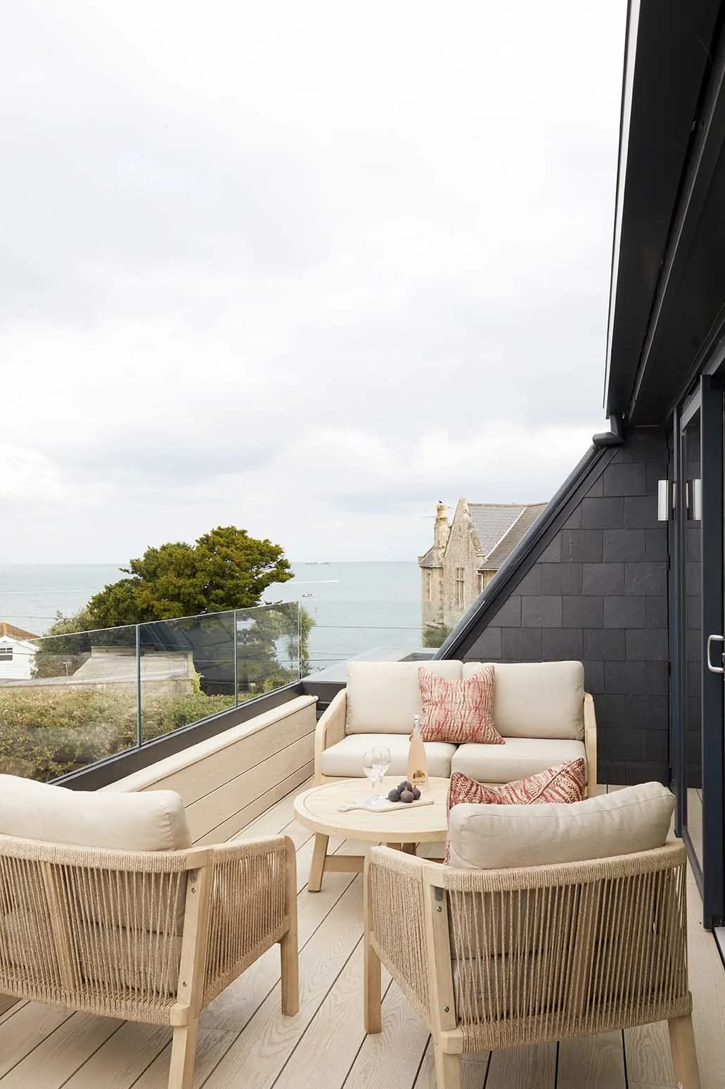 Upper-floor roof terrace with glazed balustrade, pale outdoor lounge furniture and panoramic sea views from the renovated coastal home in Seaview.