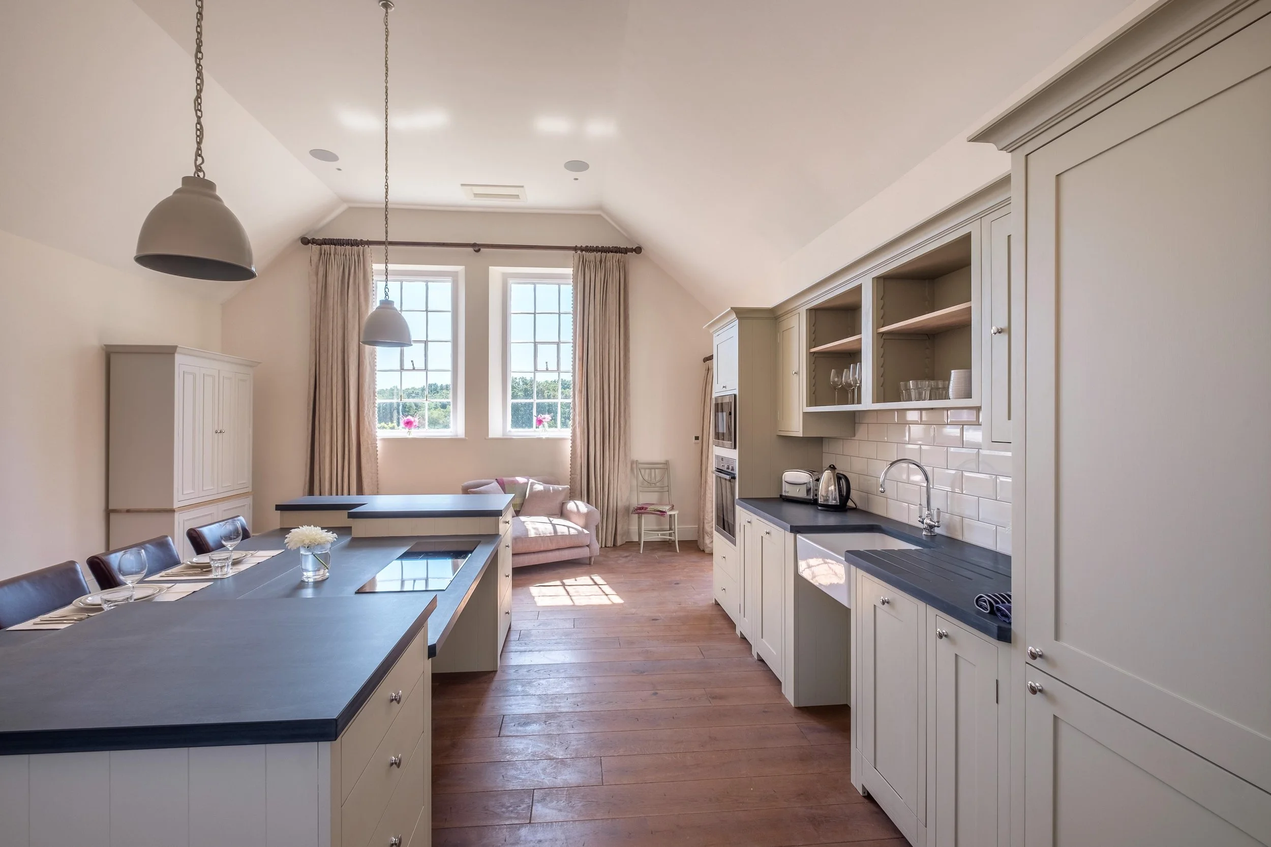 Renovated kitchen at Barton Manor Estate with pale traditional cabinetry, dark worktops, a central island and timber flooring.