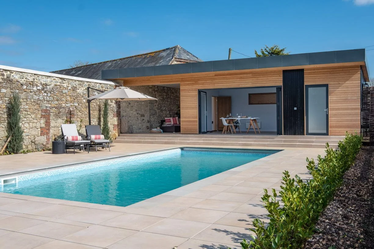 Swimming pool and landscaped grounds at Wacklands Farmhouse, Newchurch, Isle of Wight, showing the setting of the contemporary pool house within the wider historic estate.