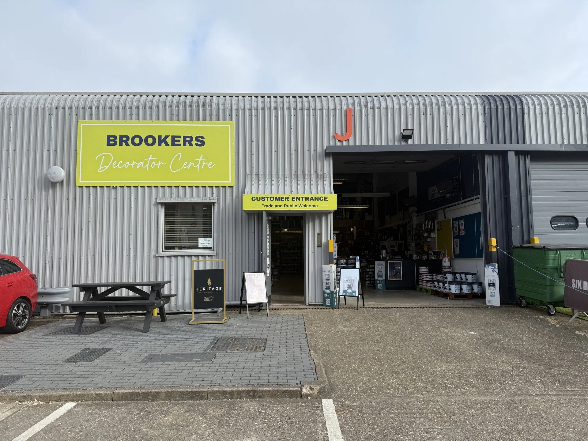 Exterior of a building with a sign for Brooker's for building and home painting and decorating supplies, showing a customer entrance and a blue garage door.