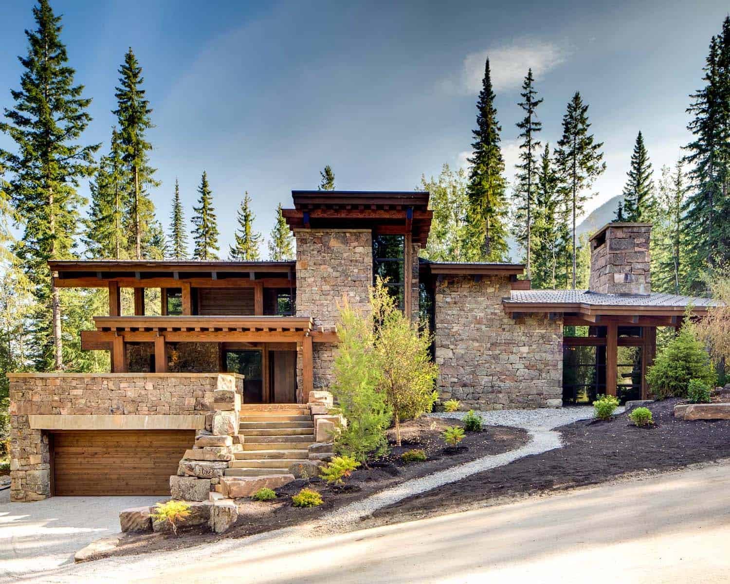 Modern mountain home built with stone and wood, surrounded by tall pine trees.