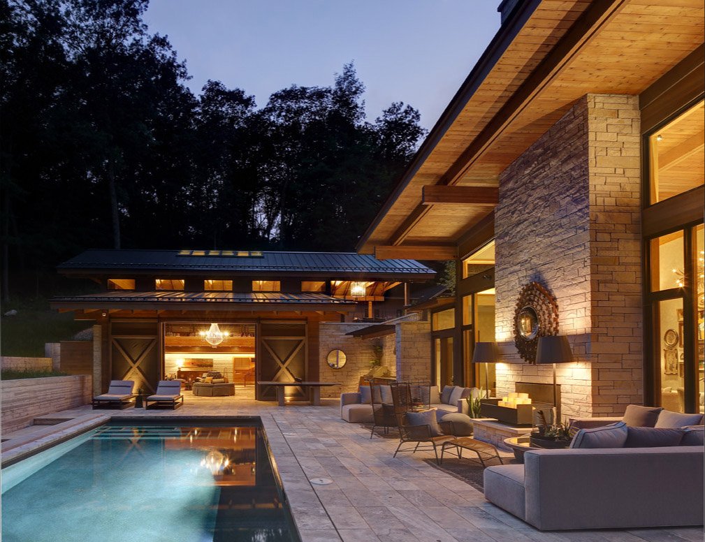 Modern luxury house with outdoor pool and patio at dusk, featuring stone architecture, large windows, and stylish furniture.