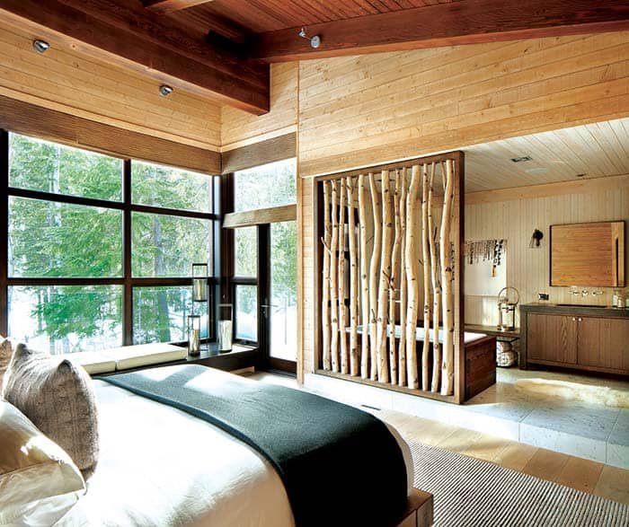 Modern rustic bedroom with large windows, natural wood paneling, and a decorative wooden room divider.