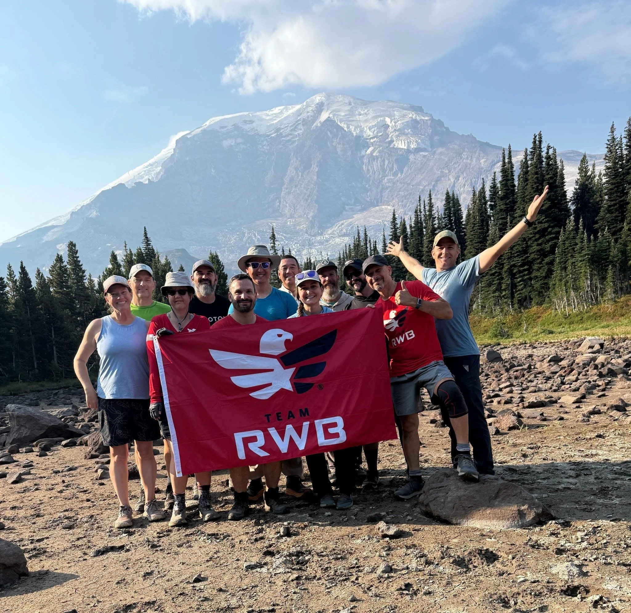 a group of veterans posing with a team rwb flag after a hike with a mountain peak behind them