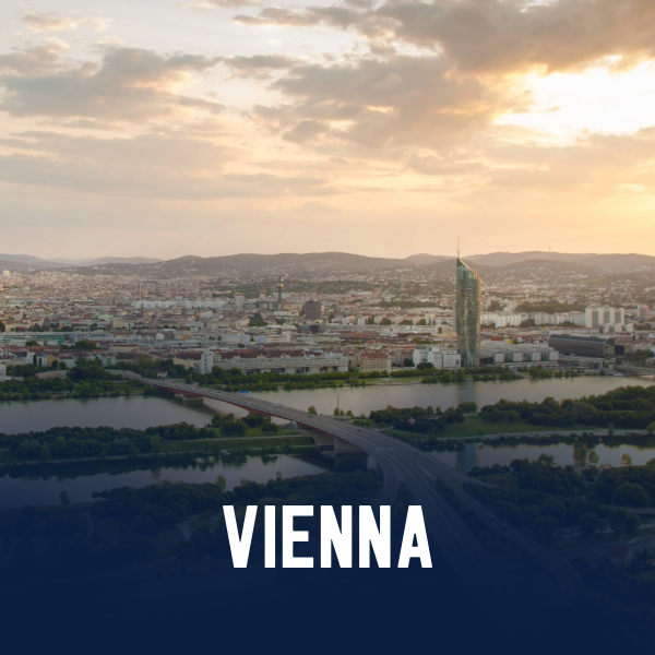 A city skyline with a river, bridge, and high-rise buildings under a partly cloudy sky during sunset in Vienna.