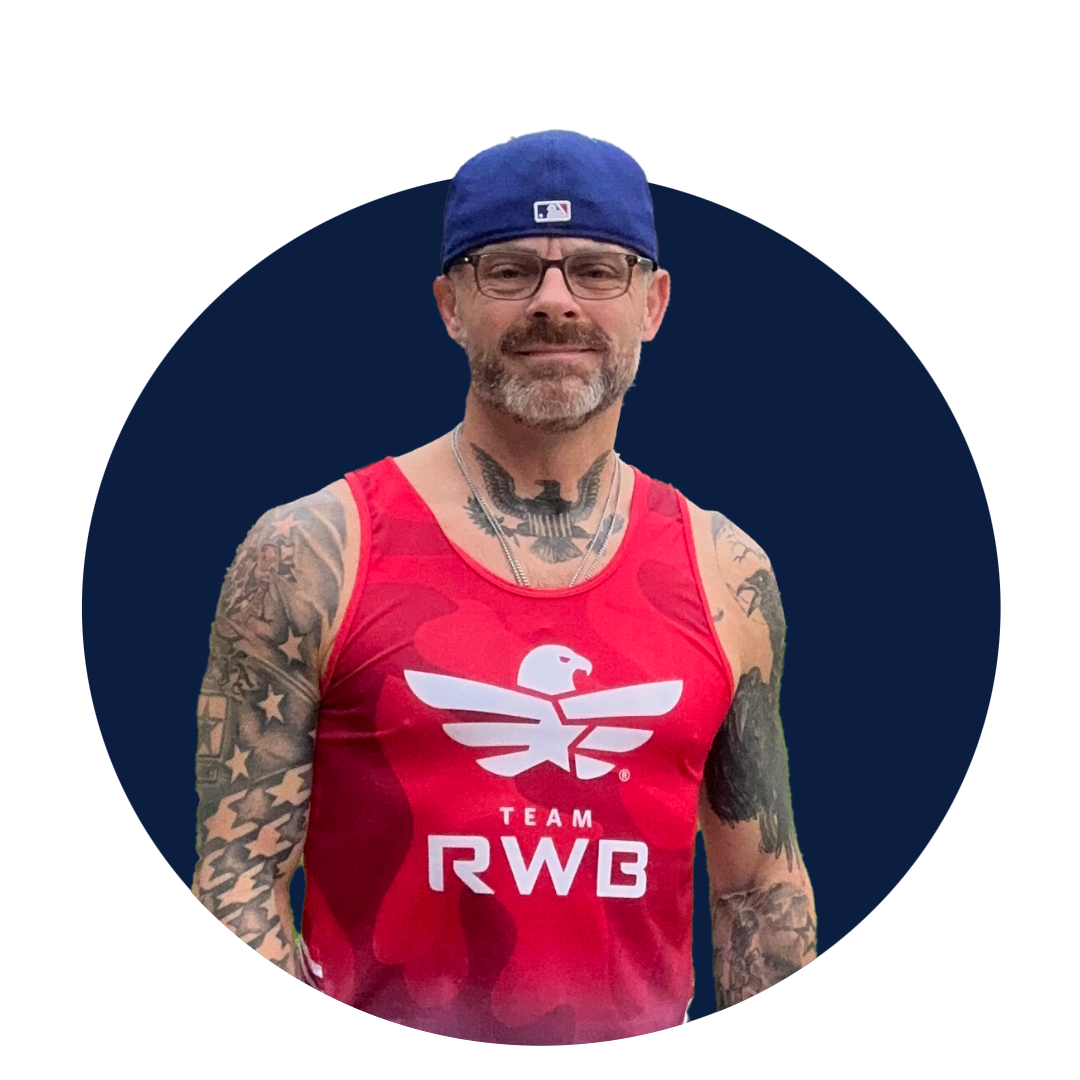 A man with tattoos wearing a red tank top with the logo and text 'Team RWB' and a blue baseball cap.