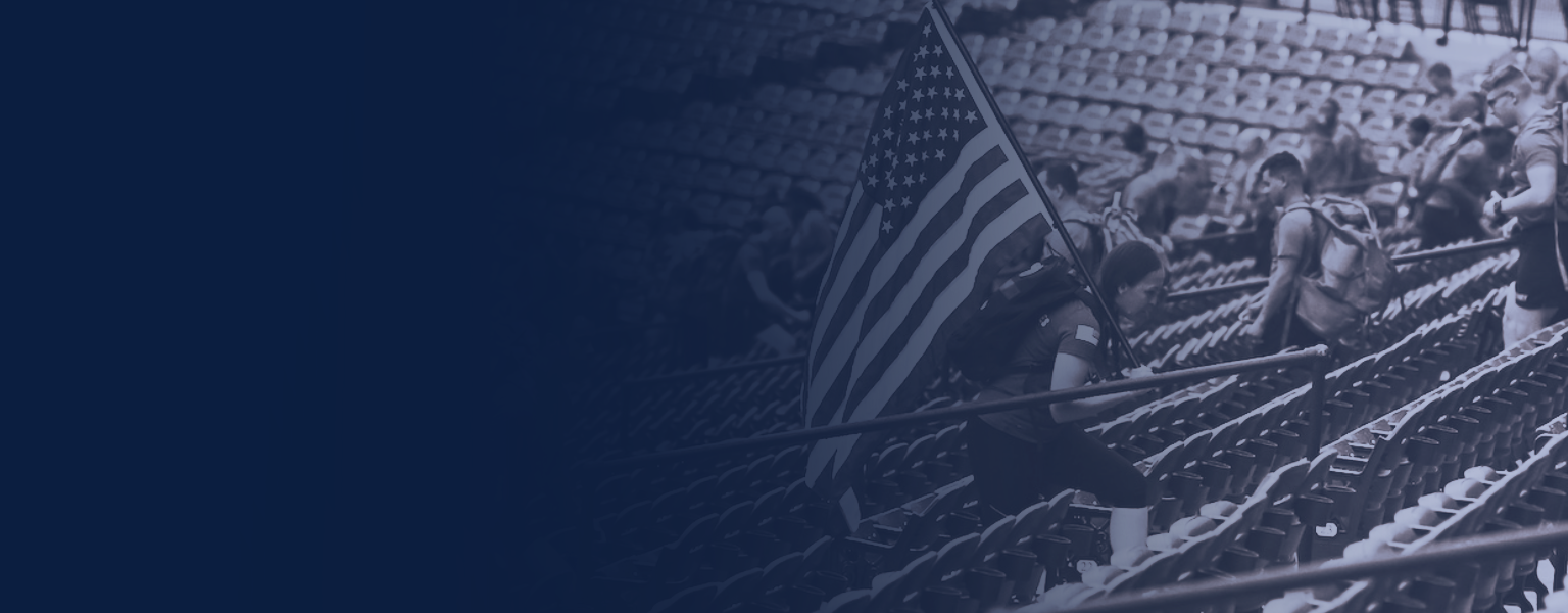 People walking up stadium stairs, some carrying backpacks, with one person holding an American flag. 