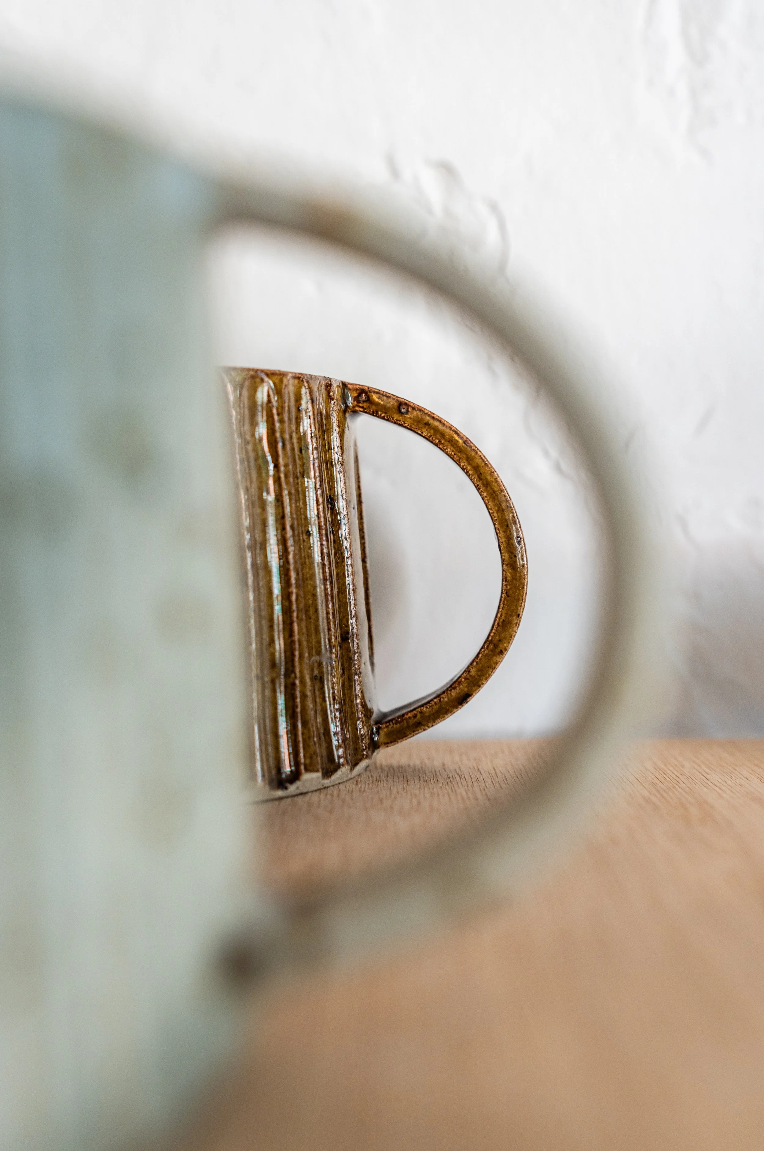 Close-up of a rusty mug seen through the hole of a ceramic object, with a plain white wall in the background.
