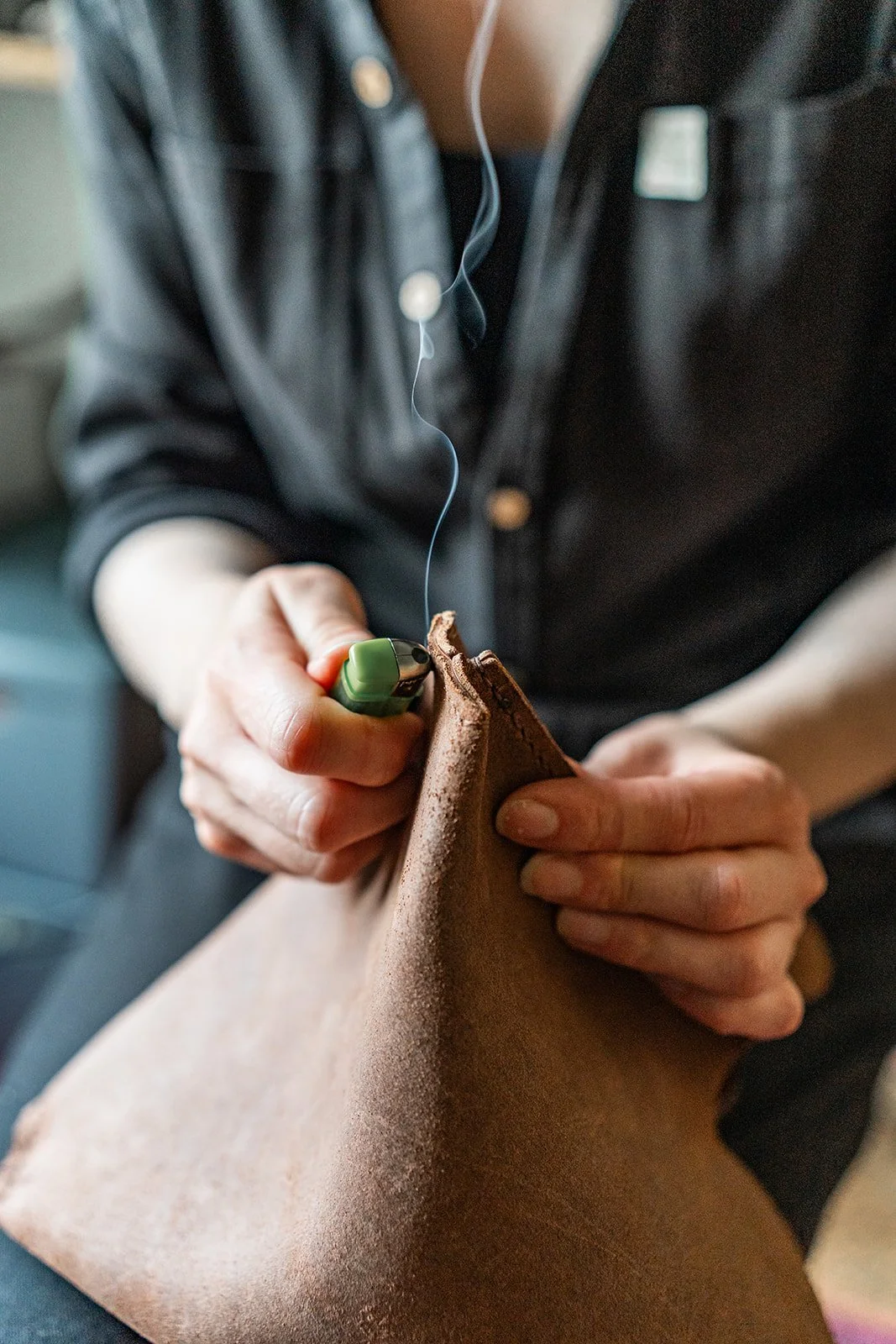 A person working on a leather piece, using a tool and wearing earphones.