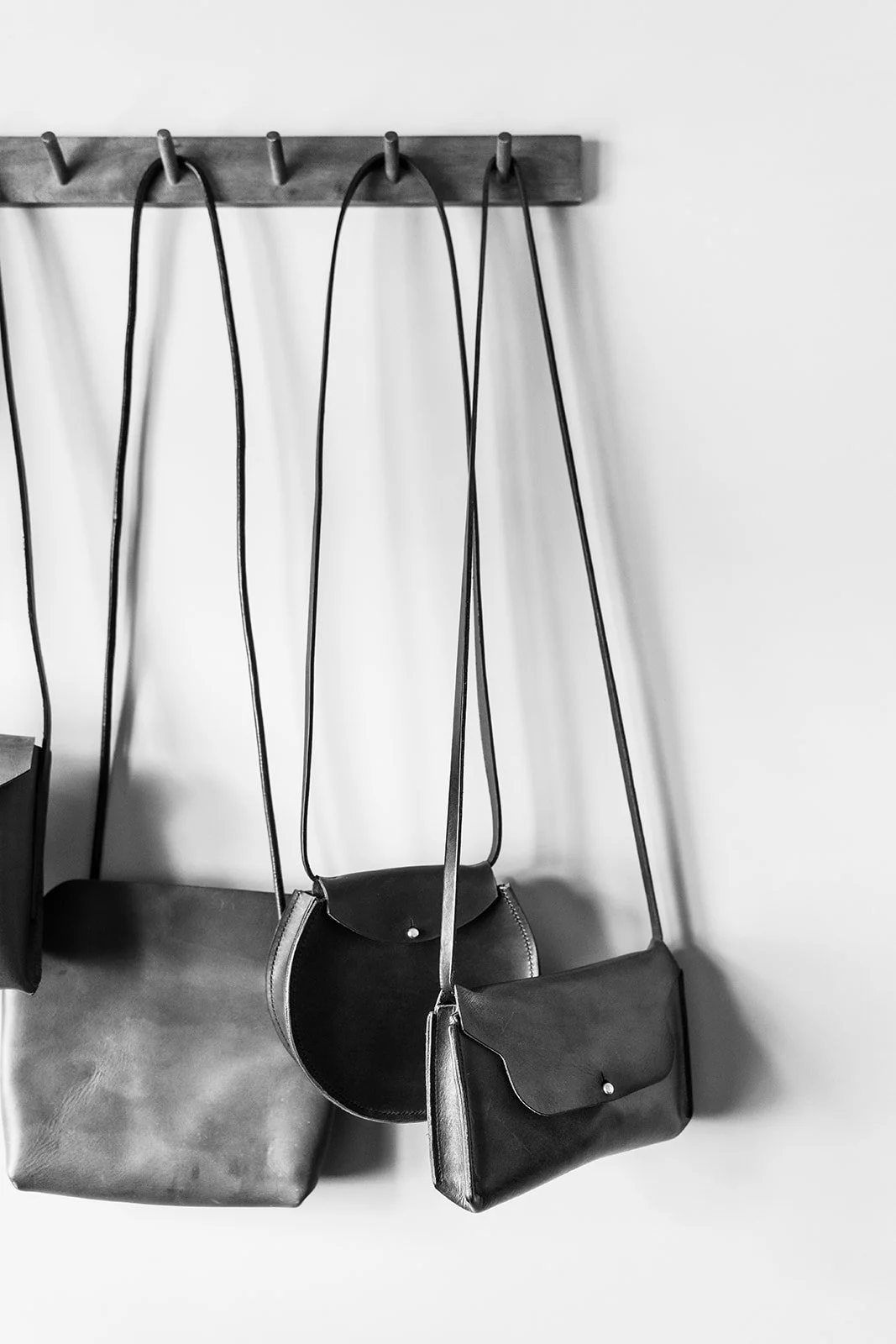 Black and gray handbags hanging on hooks on a wooden wall rack.