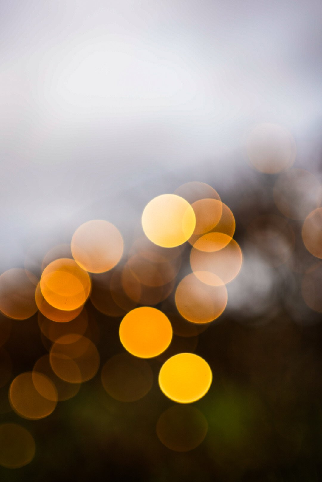 Blurred image with bokeh yellow lights on a dark background, and a hazy gray sky at the top.