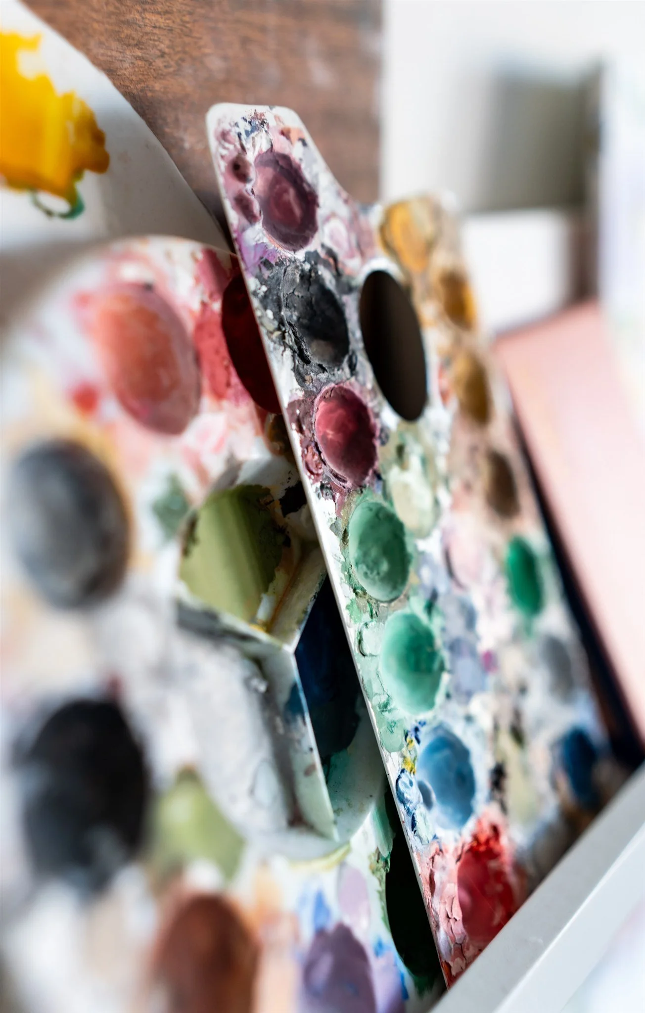 Close-up of a well-used watercolor paint palette with various colors, some mixed and dried, on a white surface.